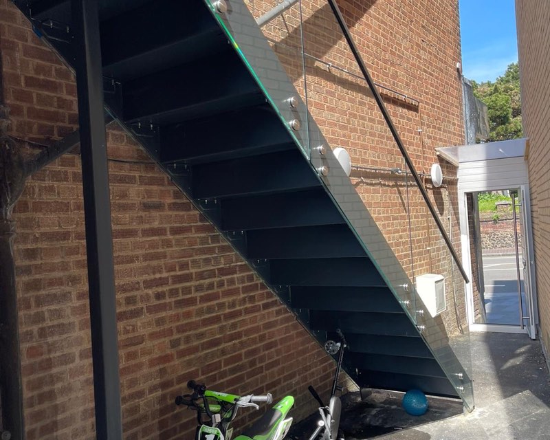 Underside of a straight black steel staircase on a single stringer against a brick wall