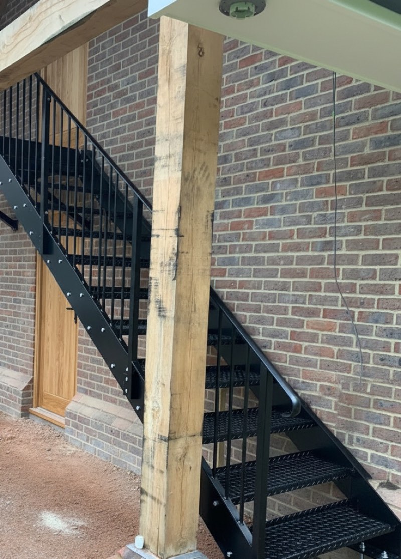 Black steel staircase with open mesh treads beneath an oak-framed porch