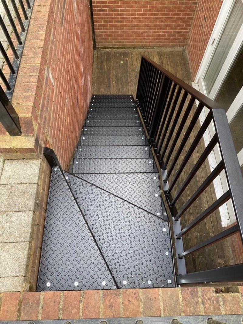 Black winder staircase with chequer-plate treads seen from above, leading down to a basement