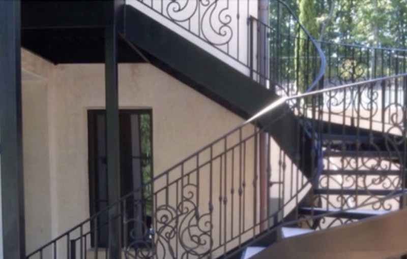 Black helical steel staircase with yellow tread nosings curving up to a first-floor landing on a brick building
