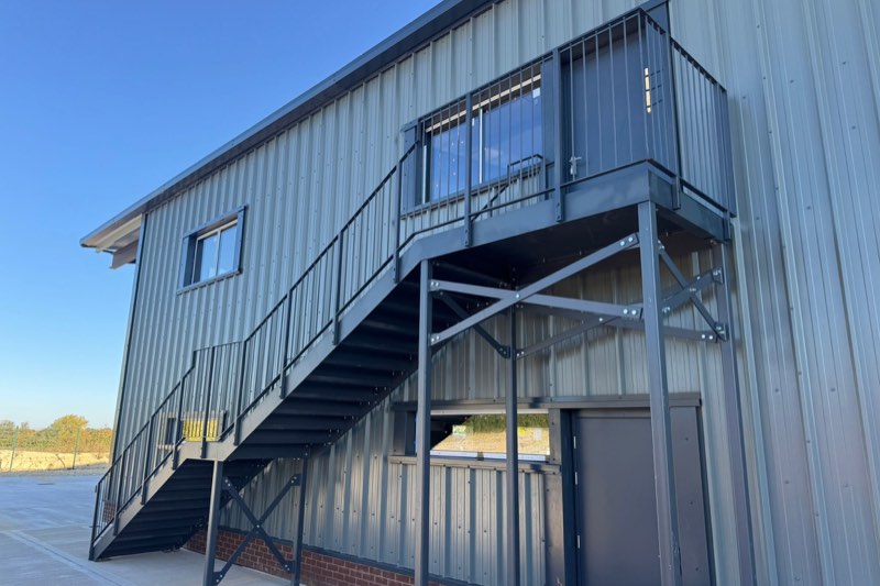 Grey powder-coated fire escape staircase with a landing on a clad industrial building