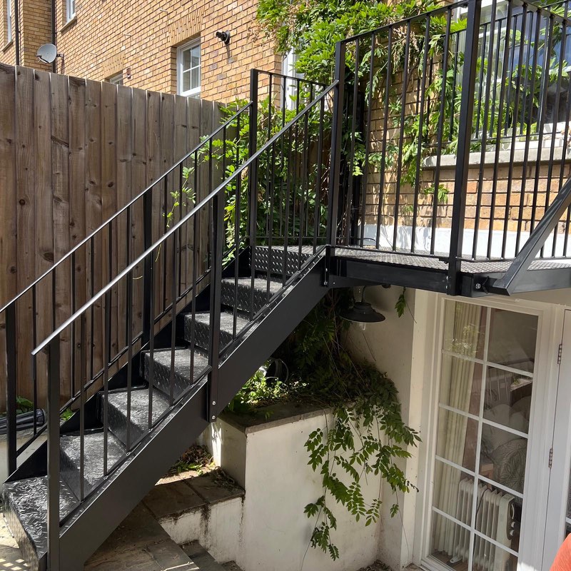 Black quarter-turn staircase with a landing leading to a lower garden and door