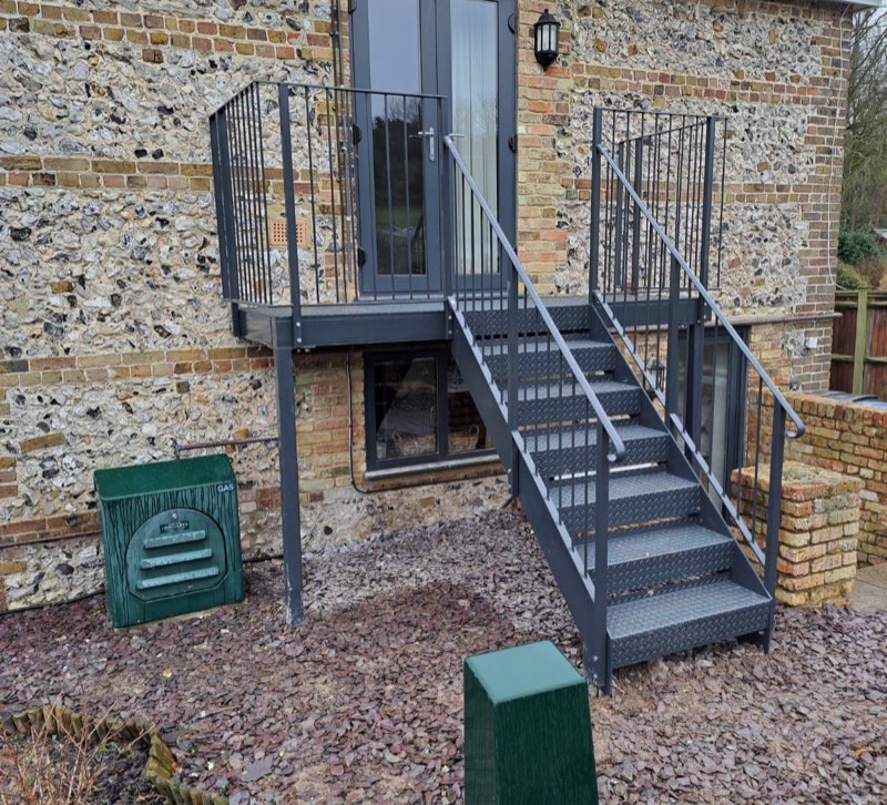 Grey powder-coated external staircase with a mid-level platform on a flint cottage